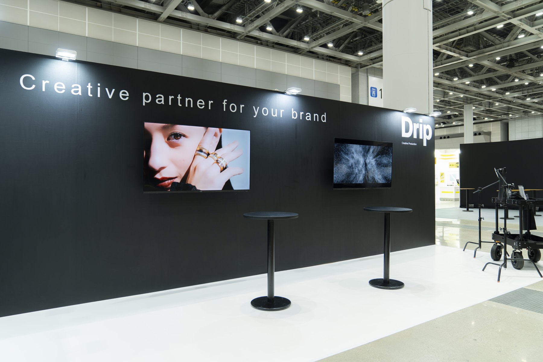2面の映像モニターとDripロゴを設置した黒い展示ブースを、会場の通路側から見た様子