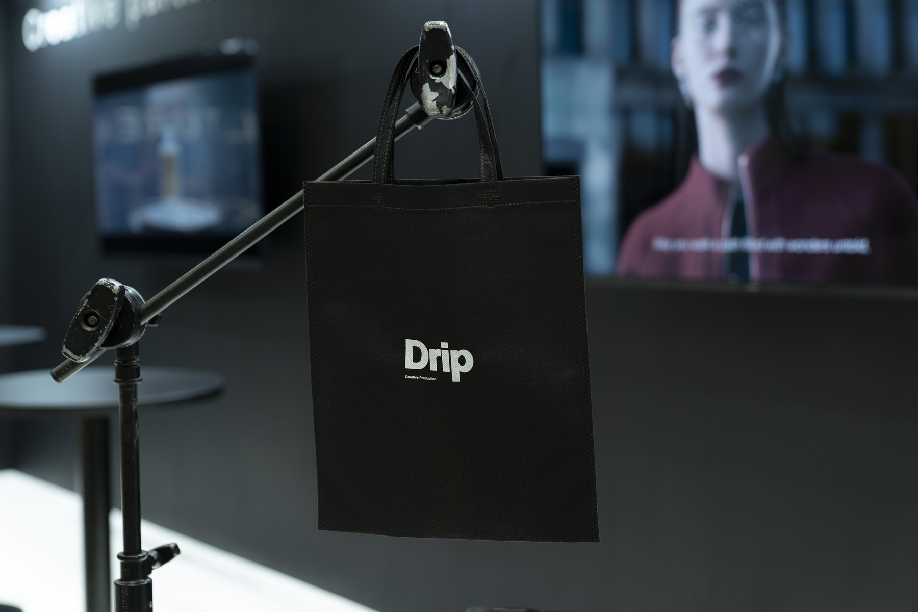 映像モニターを背景に展示した、白いDripロゴ入りの黒いトートバッグ
